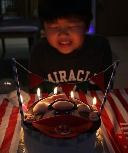 バースデーケーキのキャンドルの火を吹き消す男の子の画像